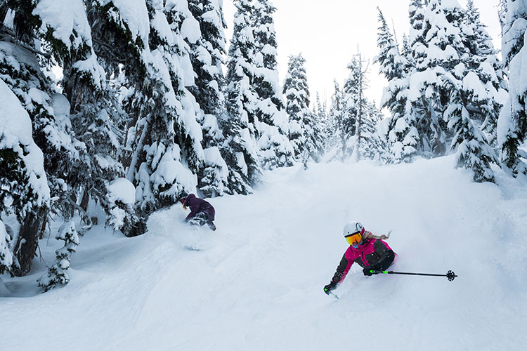 A skier and boarder power through the snow in Whistler.