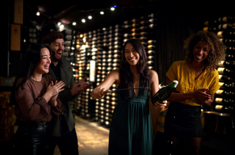 A group of friends laugh as they saber sparkling wine in the wine cellar of the Bearfoot Bistro in Whistler.