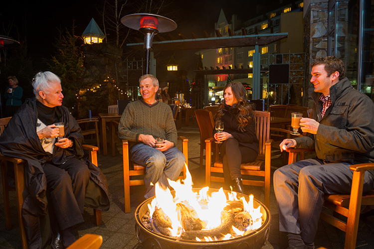 Family with drinks around a fire at Dubh Linn Gate Whistler