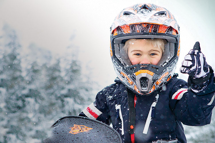 A child gives the thumbs up to the camera while snowmobiling in Whistler.