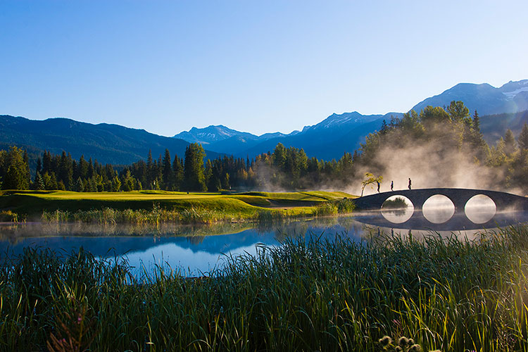 Golfers walk across a bridge in the sunshine at Whistler Golf Course.