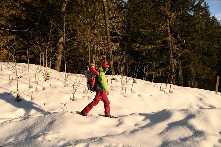 A mother carries her young baby in a backpack on a snowshoe adventure in Whistler.