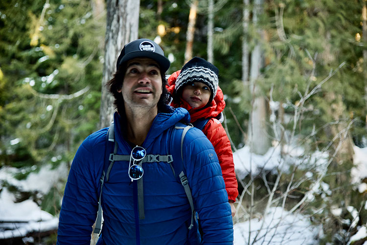 A father snowshoes with his young son in a backpack in the old-growth forest of Whistler Olympic Park.