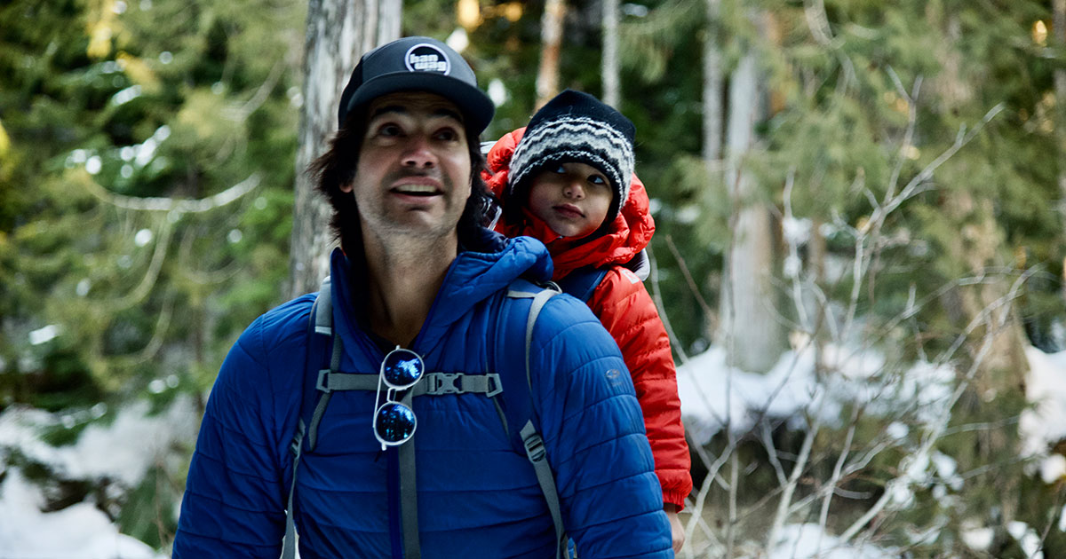 A father snowshoes with his young son in a backpack in the old-growth forest of Whistler Olympic Park.