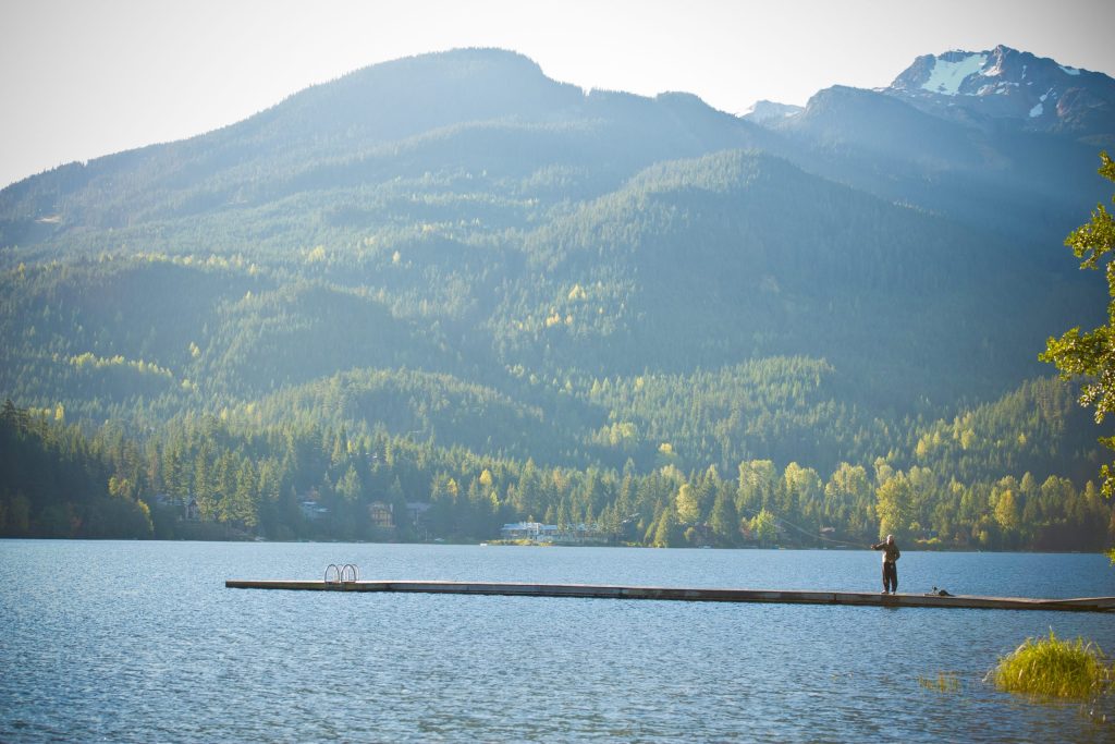 A person fishes off the dock at Rainbow Park in Whistler on a sunny, summer day. 