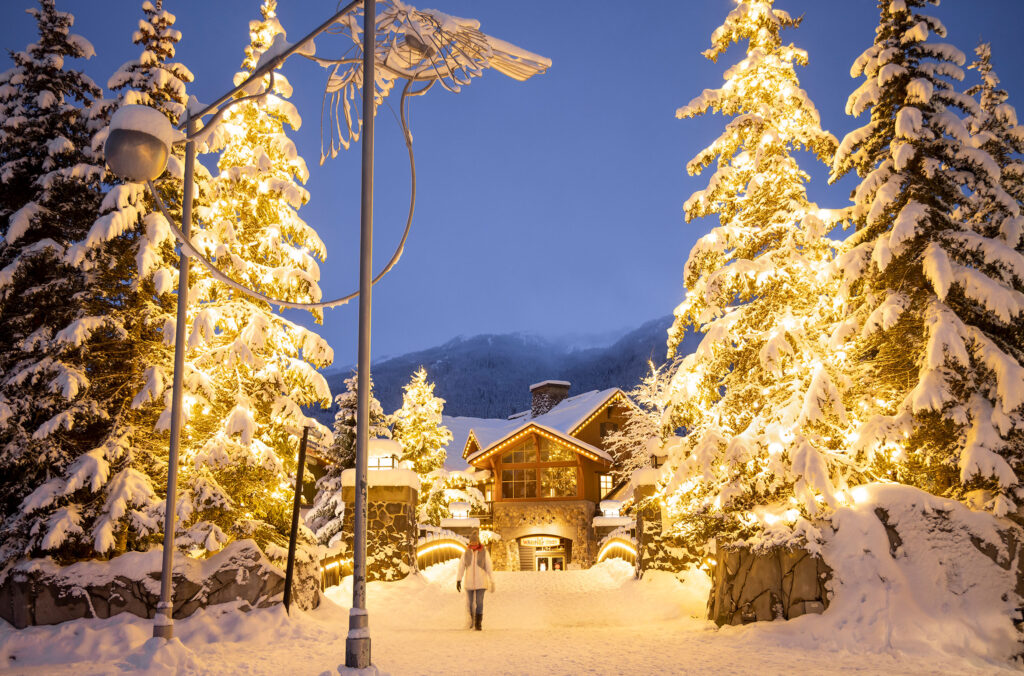 A woman walks amongst the festive lights in Creekside in the snow.