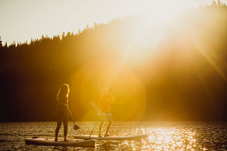 A couple stand up paddle board at sunrise on a lake in Whistler.