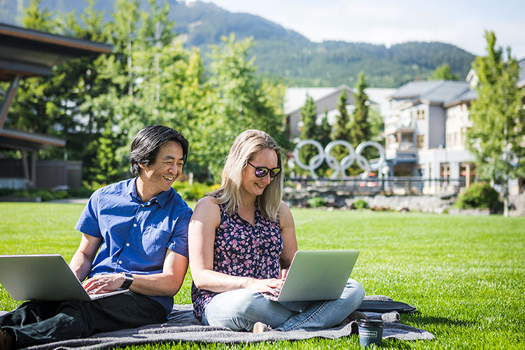 A man and woman sit in Whistler Olympic Plaza working on their laptops.