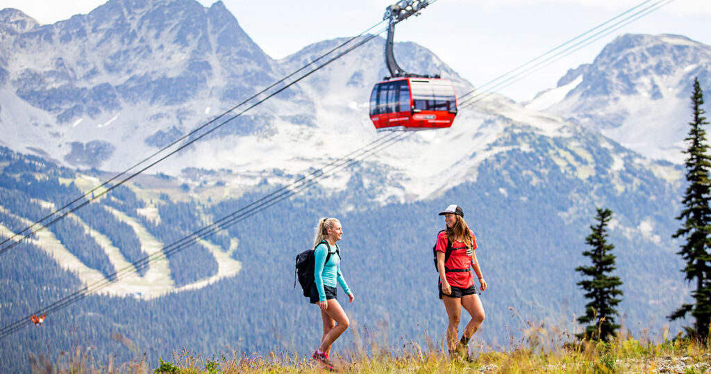 Two women hike under the PEAK 2 PEAK Gondola on Whistler Blackcomb.