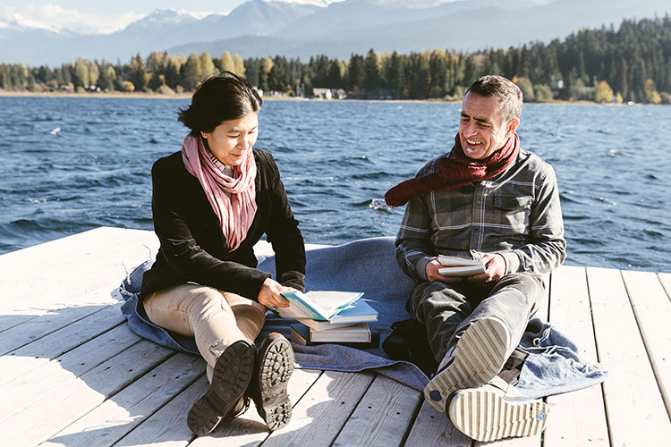 A man and a woman sit on a dock on Alta Lake in Whistler reading and discussing books.