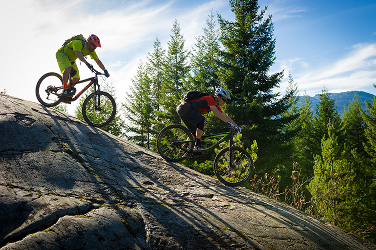 Two cyclists tackle a rock roll in Whistler.