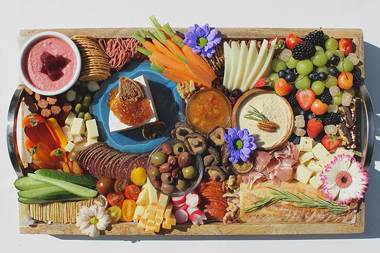 A colourful charcuterie platter with meats, cheeses, flowers, berries, chutneys and sauces.