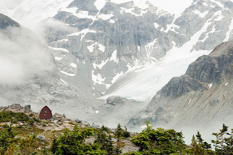 A rustic cabin sits amongst rocks and alpine shrubs at the top of the Wedgemount Lake trail in Whistler.