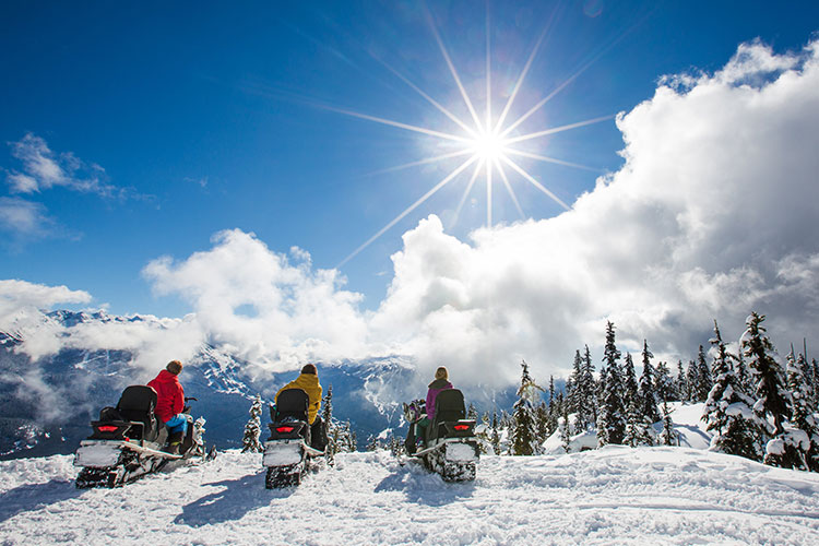 Three snowmobilers stop riding to take in the views on a sunny winter's day in Whistler's backcountry.