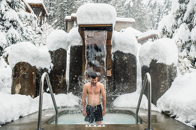 A man stands under a fountain in a cold plunge pool at the Scandinave Spa in Whistler. Snow is all around him.