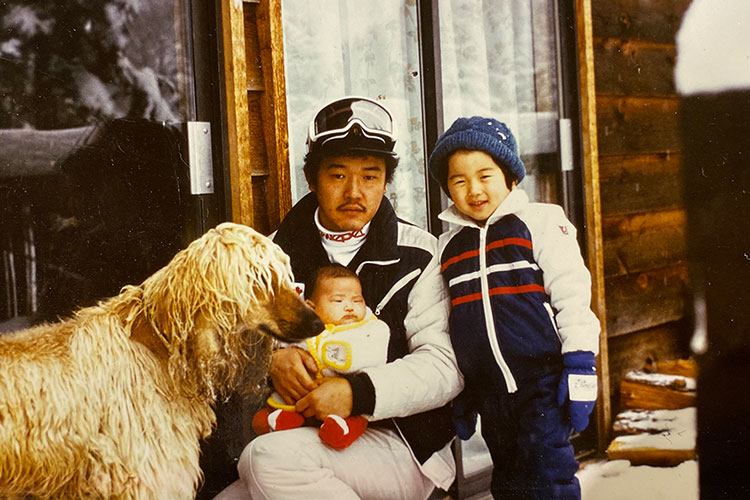 Toshi Hamazaki poses with his family, a baby girl sits on his knee while a toddler leans on his shoulder, the family dog is there too!