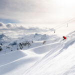 A skier in a red jacket powers down the slopes of Whistler Blackcomb in the sunshine.