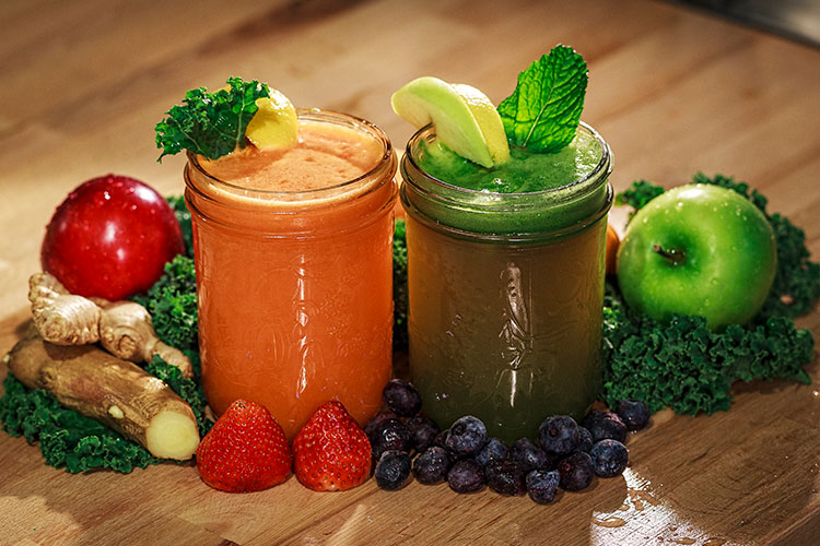 An orange and green smoothie sat amongst fruit and vegetables from the Naked Sprout in Whistler.