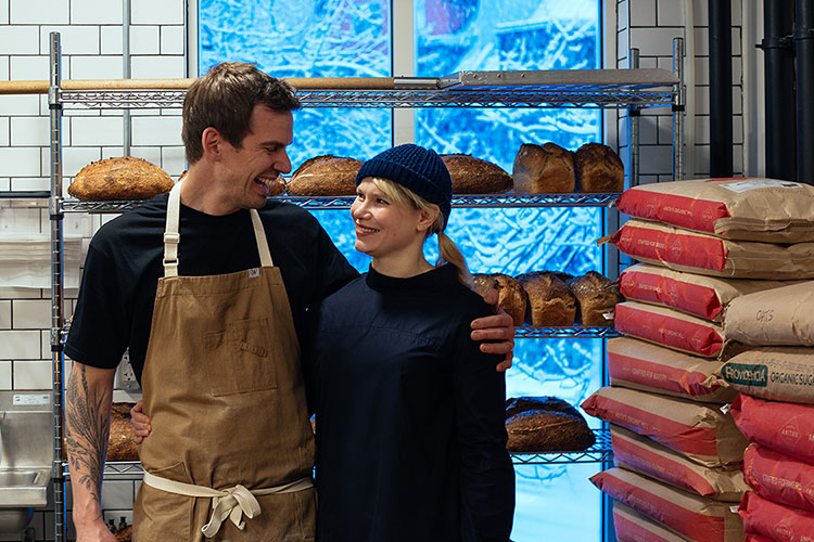 Ed and Natasha Tatton from Eds BrEd hug each other in front of a rack of sourdough.