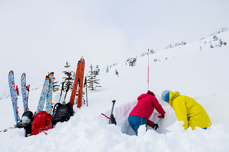 Two backcountry skiers dig a snow pit.