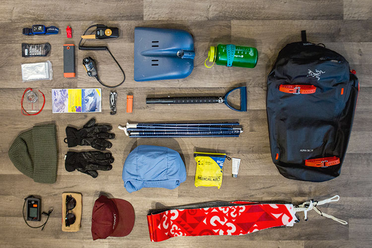 An aerial view of a backpack and it's contents, all things you need to venture into the backcountry in winter.