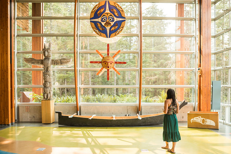 A woman looks up at artwork above a canoe at the Squamish Lil'wat Cultural Centre.