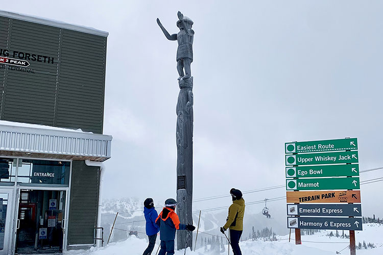 Three skiers look up at the welcome figure on Whistler Mountain.