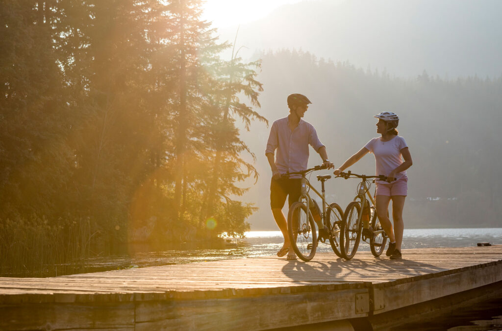 A couple walk their bikes onto a lakeside dock in the summer's sun in Whistler.