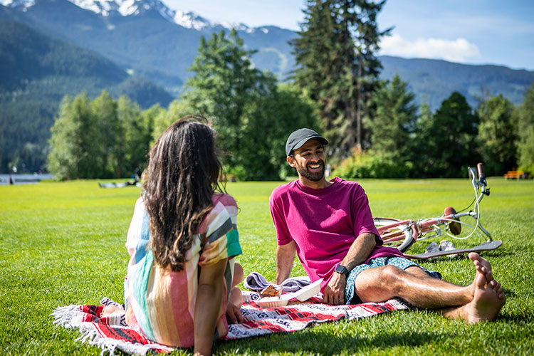 A couple hang out on the grassy lawn of a Whistler lake in summer.