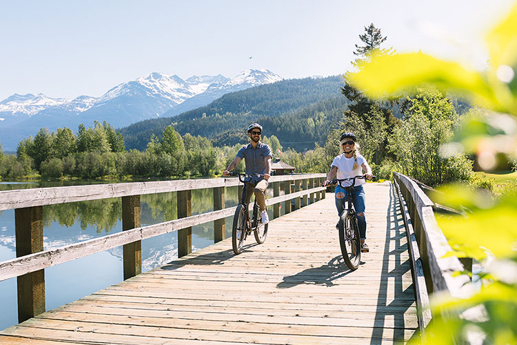 A man and a woman bike along the Whistler Valley Trail boardwalk at Green Lake.