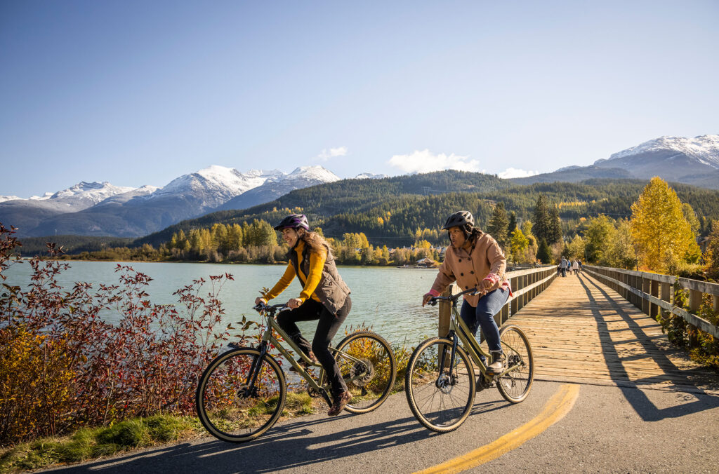 Two bike riders make their way along the Whistler Valley Trail enjoying the fall colours and views over Green Lake.