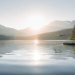 A person dives off the edge of a dock into the mirror-like waters of a Whistler lake in the summer sun.