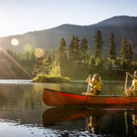 A couple canoes across Alpha Lake in Whistler as the sun hits the water.
