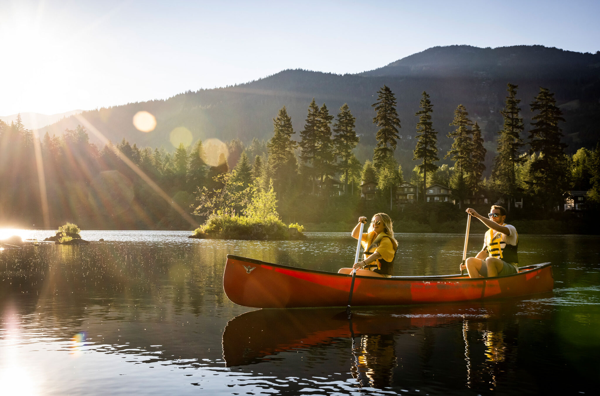 A couple canoes across Alpha Lake in Whistler as the sun hits the water.