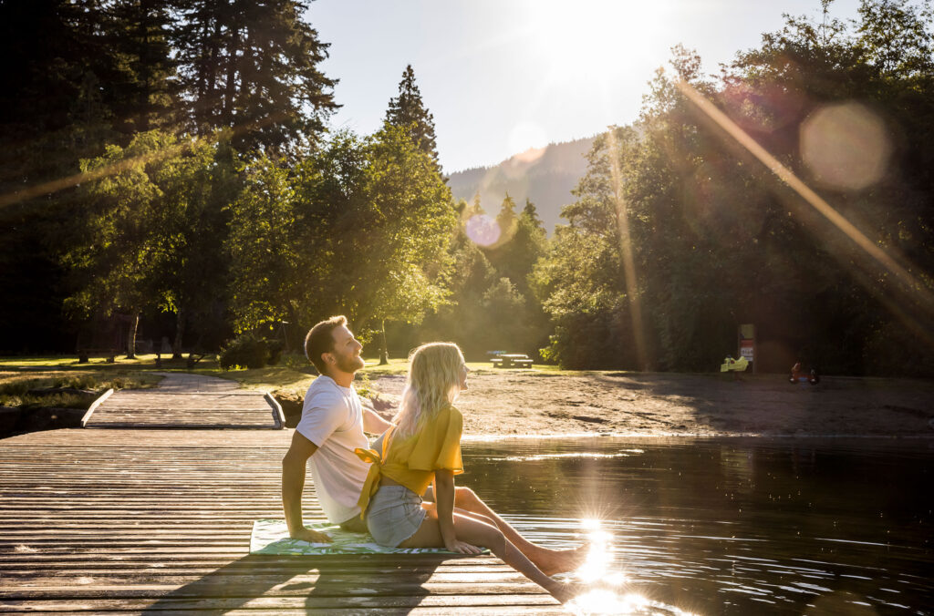 A couple sit on a dock at Alpha Lake in Whistler, basking in the summer sunshine.