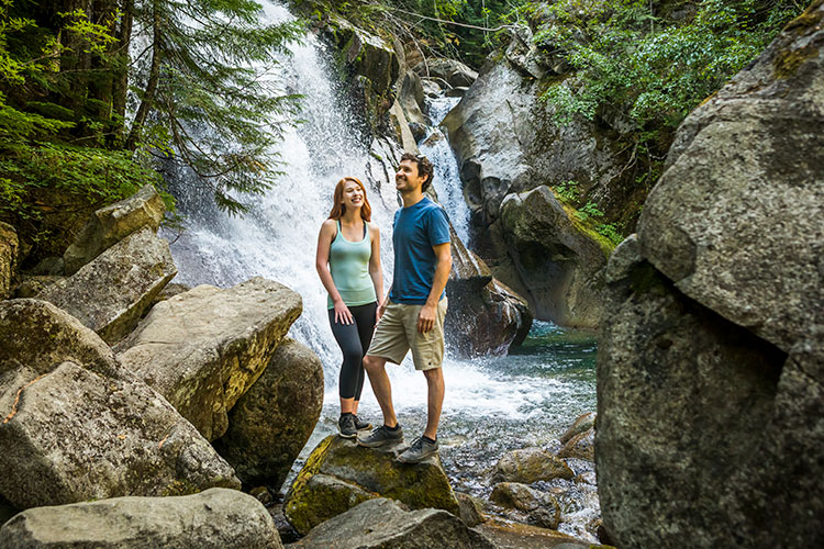 A couple stand at the base of Rainbow Falls in Whistler.