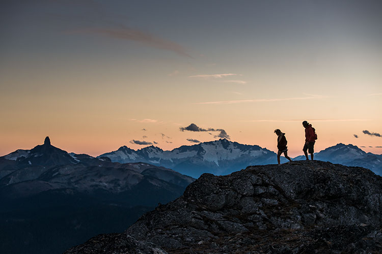 A couple hike high in the Coast Mountains with Black Tusk in the background as the sun sets in Whistler.