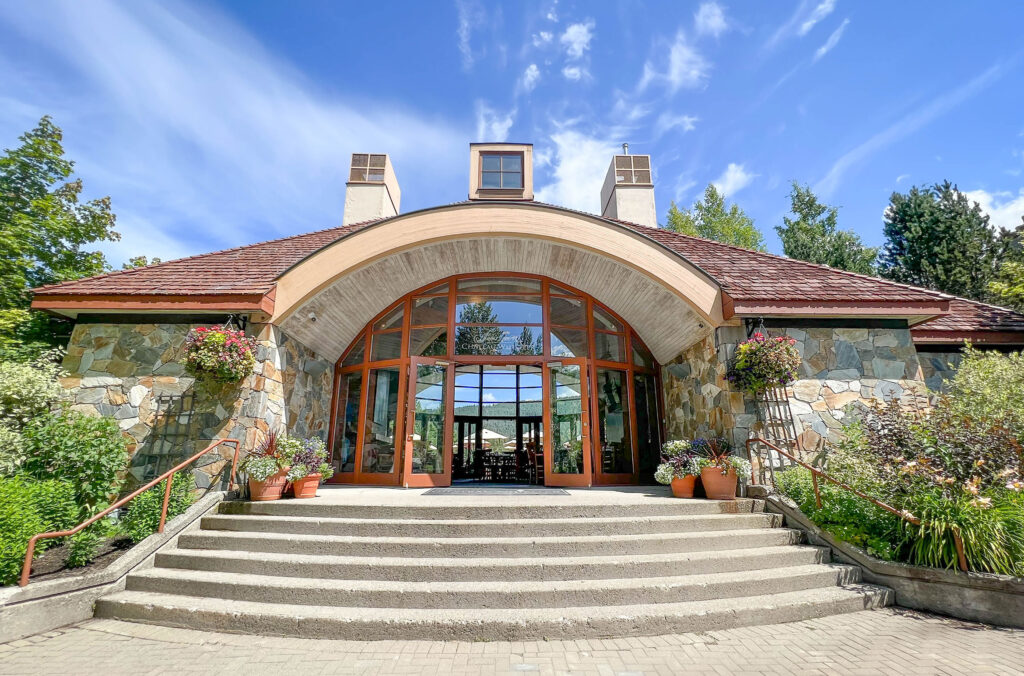 A front view of the clubhouse with open glass doors and framed by summer flowers.