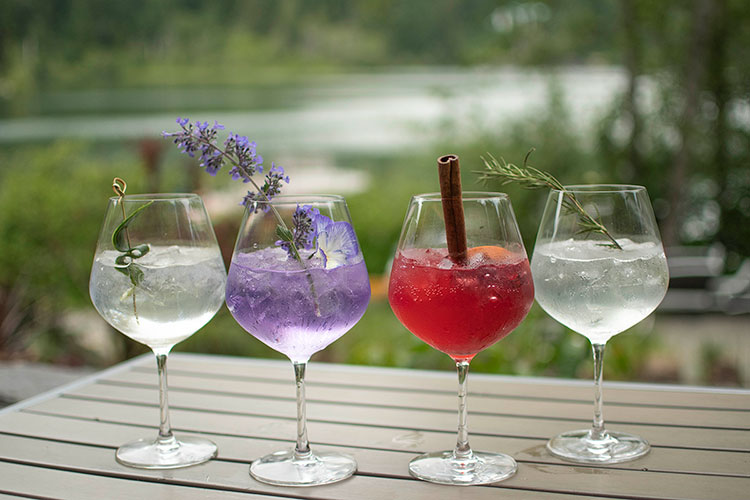 A row of gin and tonic cocktails with a lake backdrop at The Cure Lounge in Whistler.