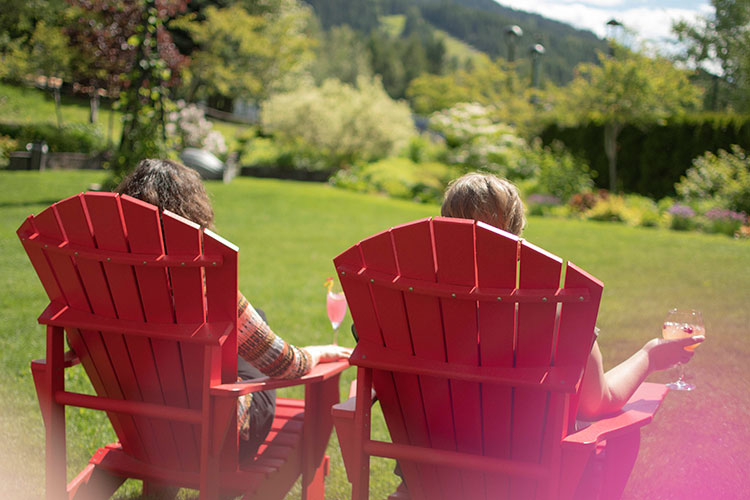 Two women sit in large deck chairs in the gardens of the Fairmont in Whistler, with cocktails in hand.