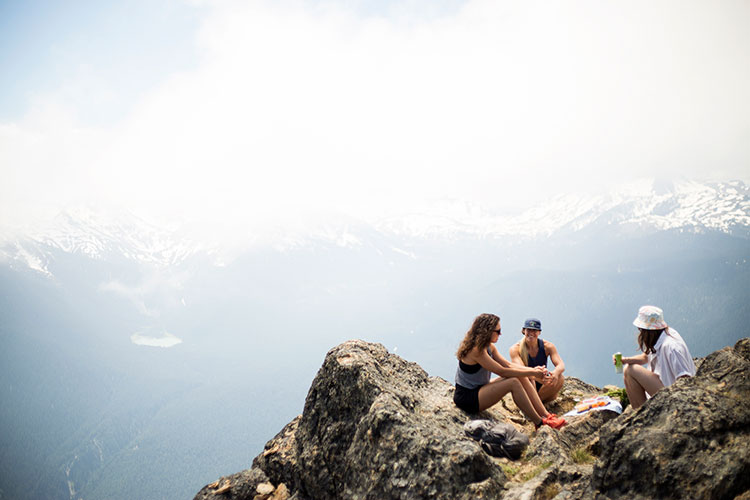 Three hikers sit on the rocks with incredible views of the Coast Mountain all around them on Whistler Blackcomb.