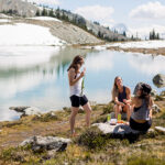 Three hikers have a picnic on the shores of an alpine lake on Whistler Blackcomb.