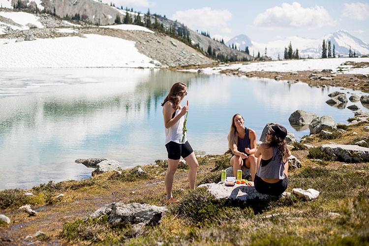 Three hikers have a picnic on the shores of an alpine lake on Whistler Blackcomb.