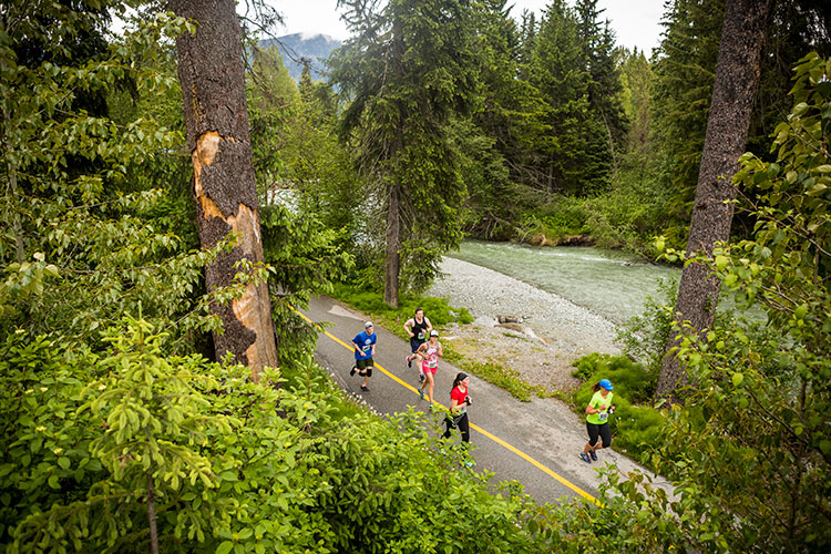 Runners head down the Whistler Valley Trail between a river and the forest in the Whistler Half Marathon.