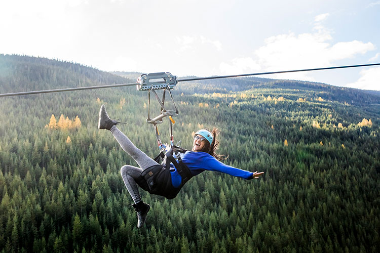 A woman zips across the Whistler Valley on a zipline, the fall forest underneath her.