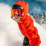 A snowboarder looks directly at the camera as they complete a powdery turn on Whistler Blackcomb.
