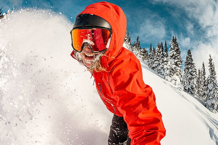 A snowboarder looks directly at the camera as they complete a powdery turn on Whistler Blackcomb.