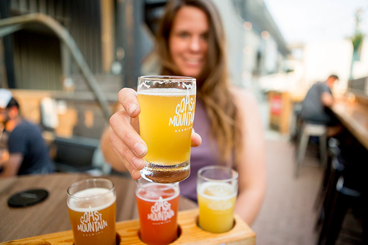 A woman holds up one of her samples from a flight of beers at Coast Mountain Brewing in Whistler.