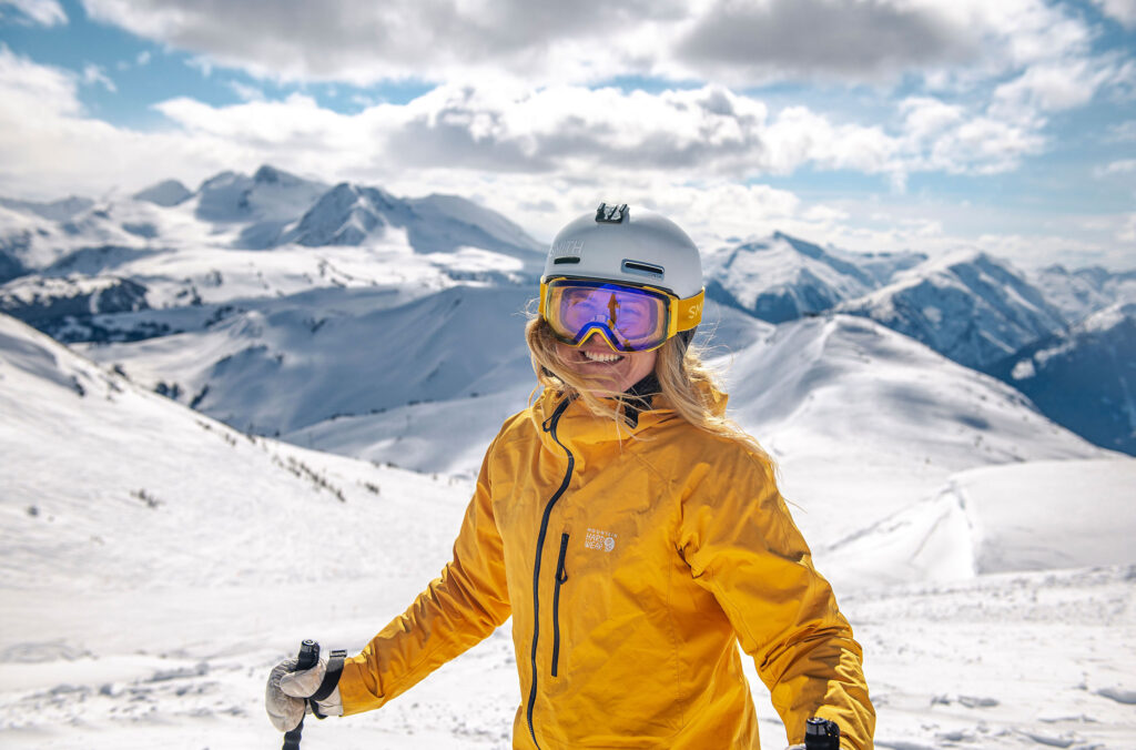 A skier looks direct to the camera, smiling on a sunny day spent on the slopes of Whistler Blackcomb.