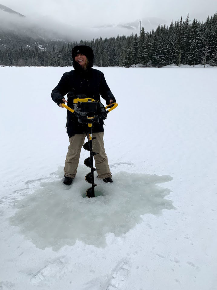 A person drills a small hole into the ice on a lake to fish in winter.